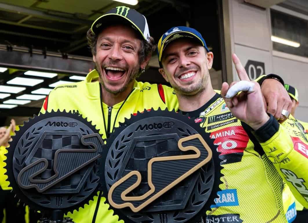 Dua pembalap MotoGP merayakan kemenangan dengan trofi dan senyum lebar.